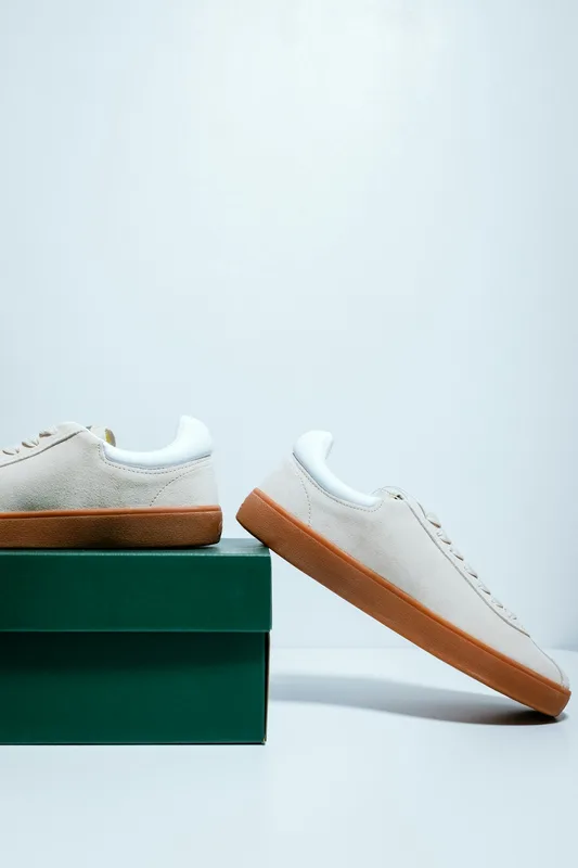 Zapatillas blancas de ante con suela de goma sobre una caja verde