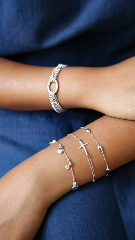 Brazos con una pulsera ancha y tres pulseras finas de plata sobre tela azul